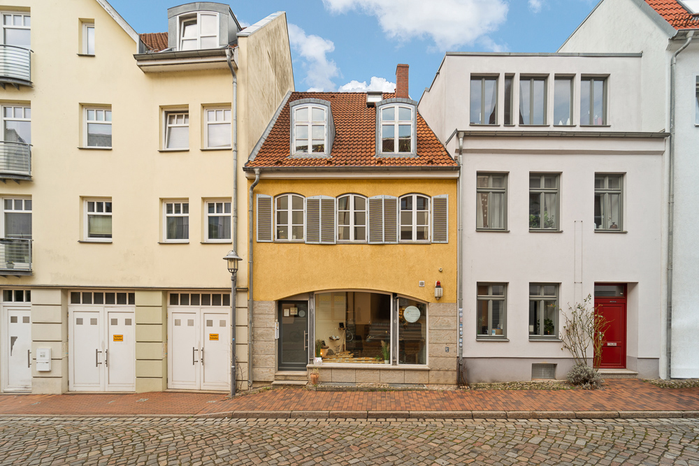 Gelbes Wohnhaus mit roten Dachziegeln und großen Fenstern in einer Häuserreihe.
