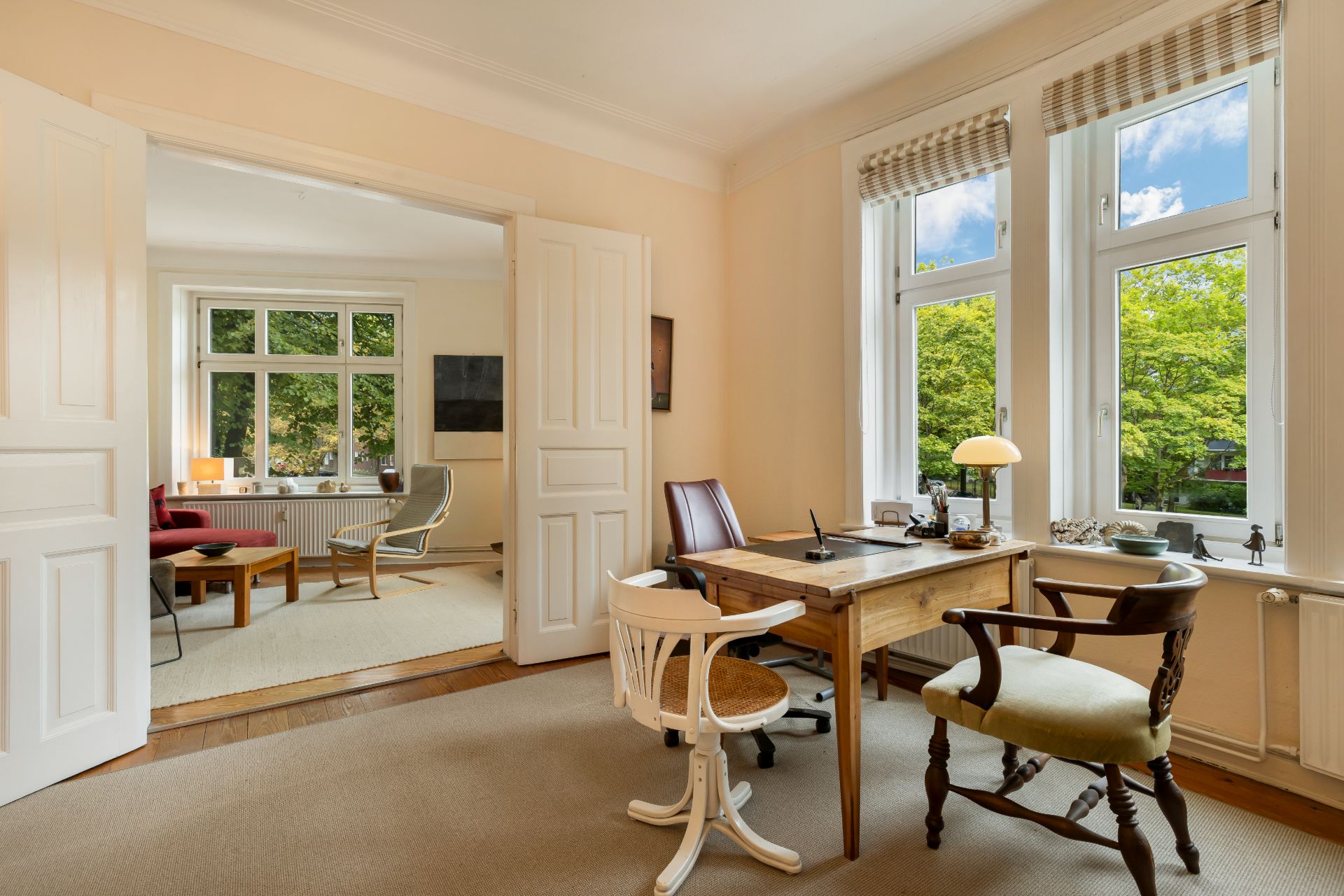 Helles Arbeitszimmer mit Schreibtisch, drei Stühlen und Blick durch Doppeltür ins Wohnzimmer.