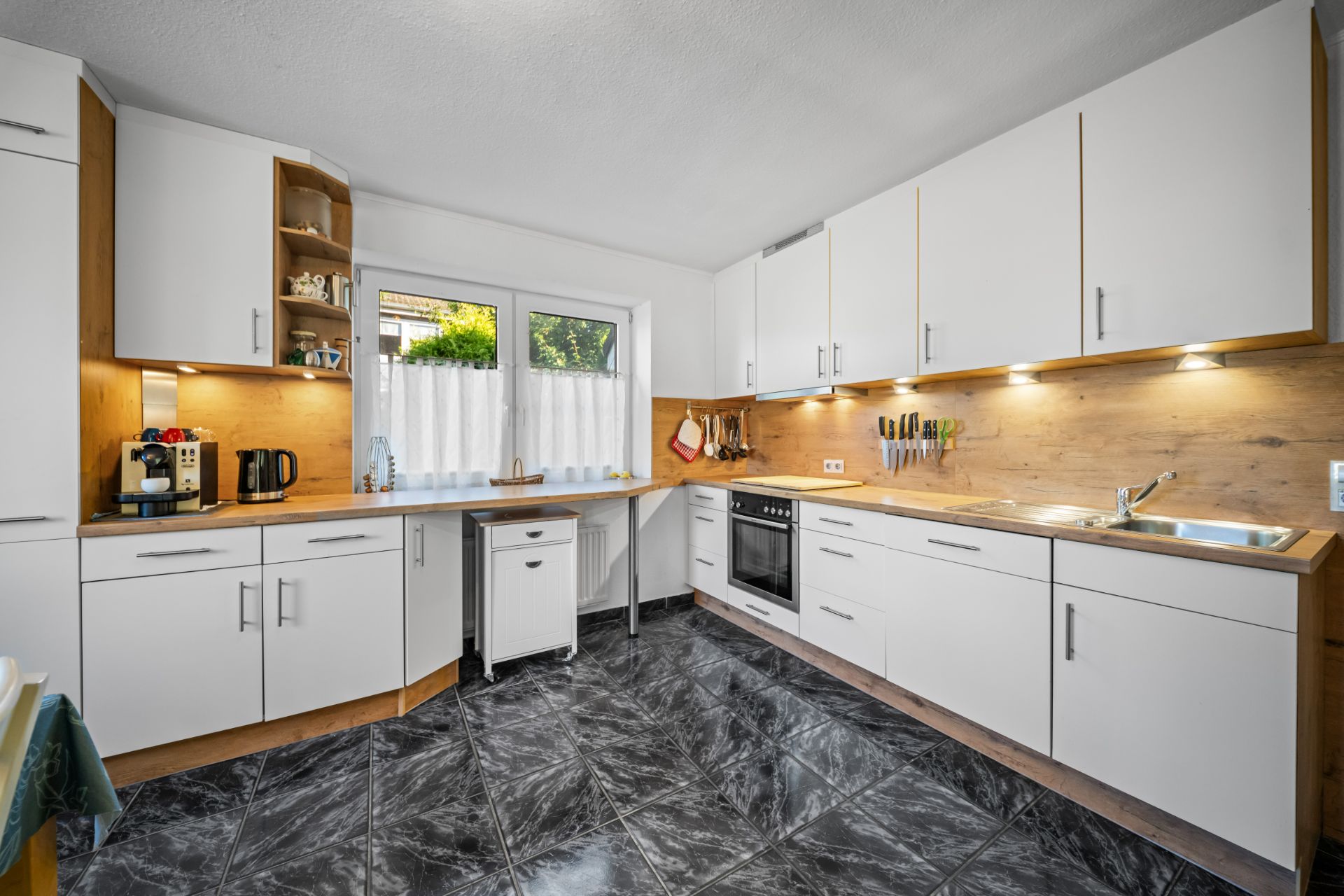 Helle, moderne Einbauküche mit weißen Schränken, Elektrogeräten und großem Fenster.