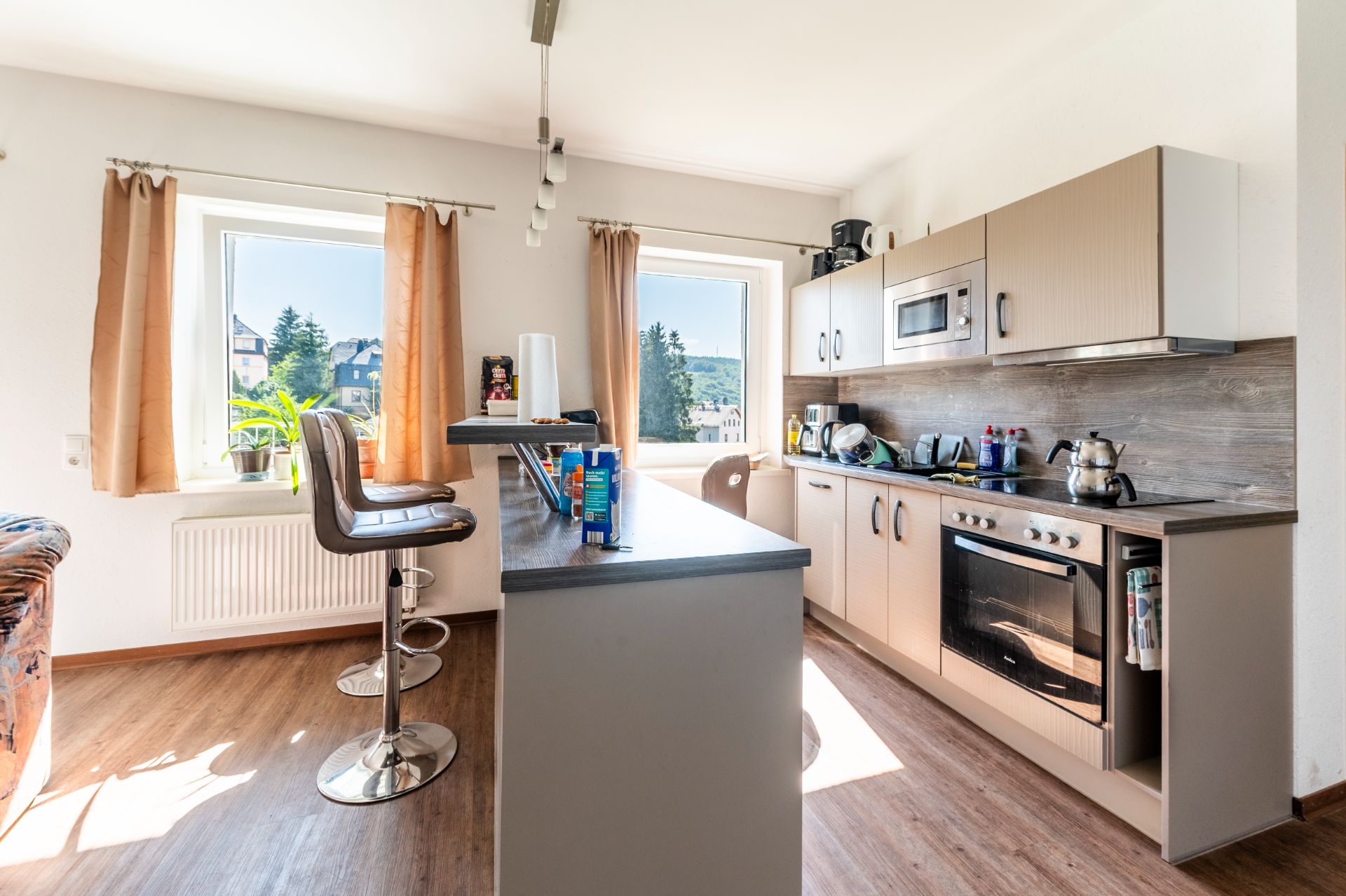 Moderne Küche mit Tresen, Barhockern, zwei Fenstern und hellen Vorhängen.
