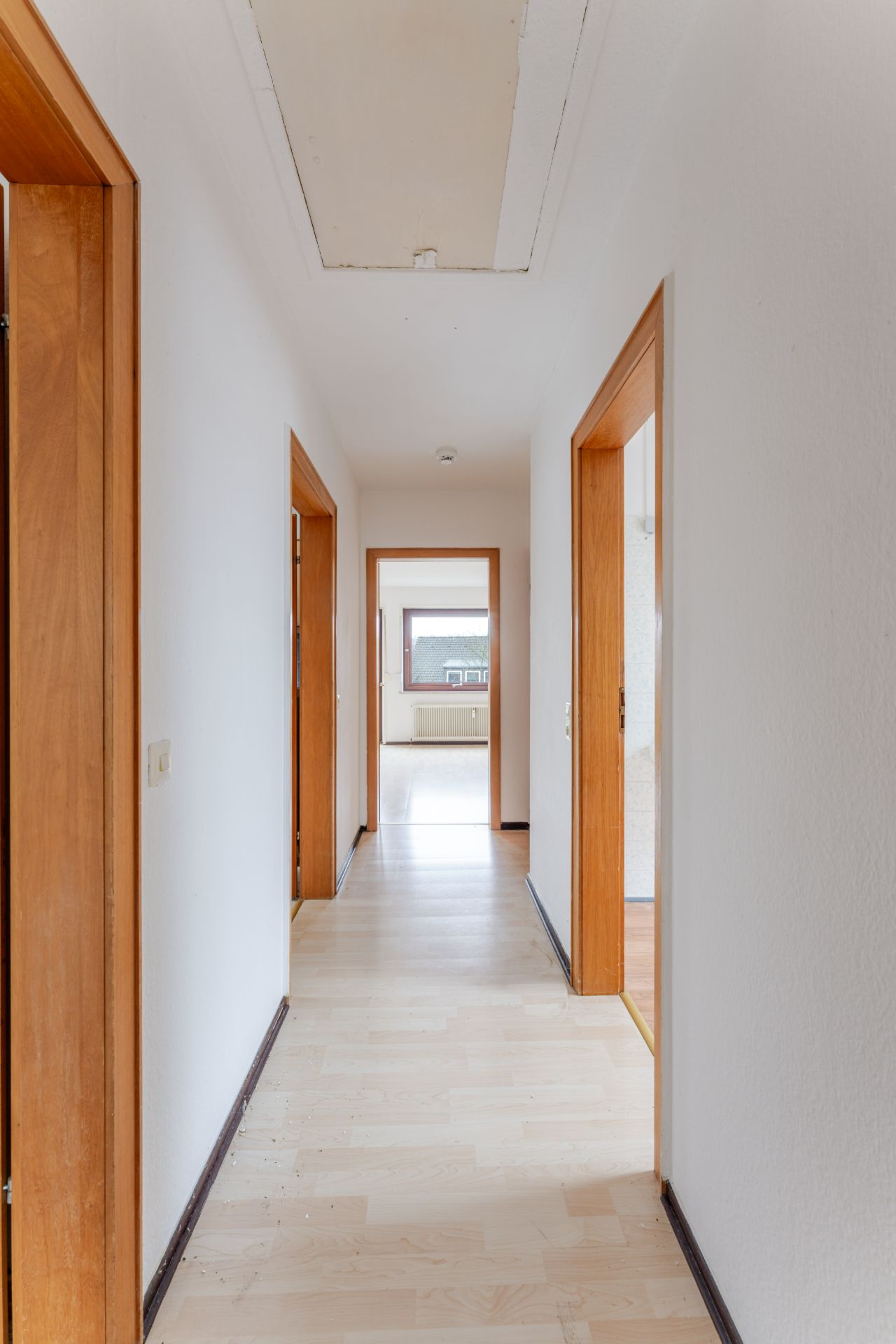 Heller Flur mit Holztüren und Blick in ein Zimmer mit Fenster.
