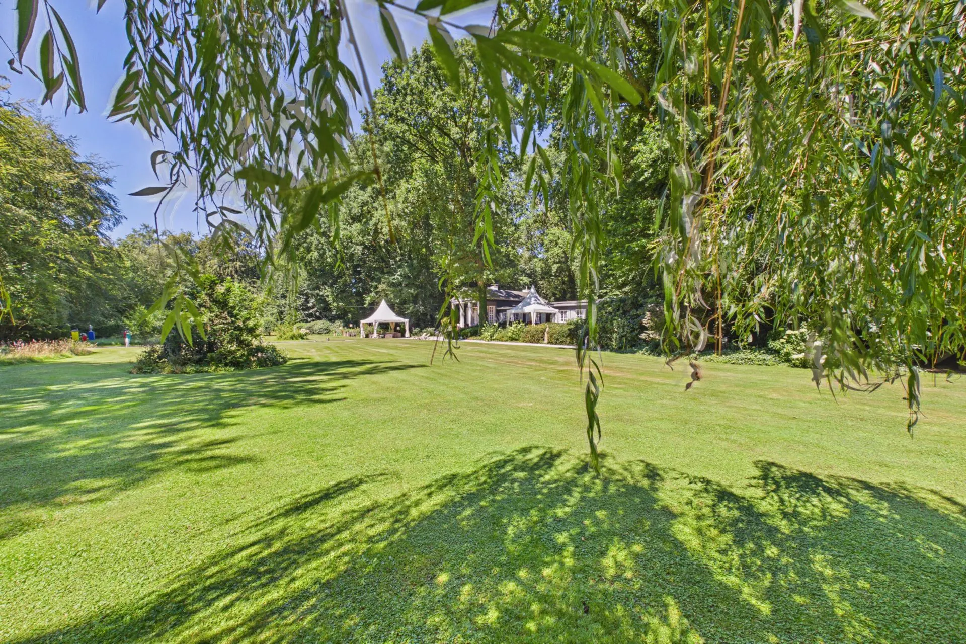 Großer grüner Garten mit Rasen, Bäumen und einem weißen Pavillon im Hintergrund.