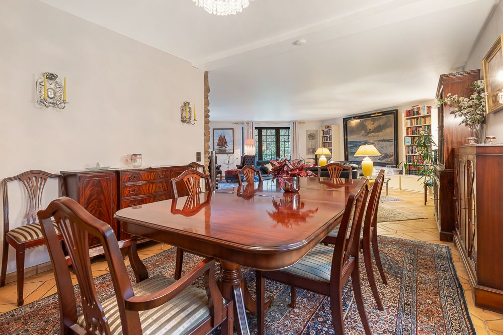 Esszimmer mit Holztisch und Stühlen, Teppich und Blick ins helle Wohnzimmer mit Sofas und Büchern.
