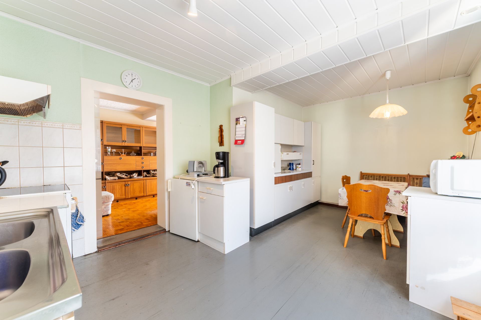 Helle Küche mit Esstisch, Stühlen, Kühlschrank und Küchenzeile, Blick in ein weiteres Zimmer.