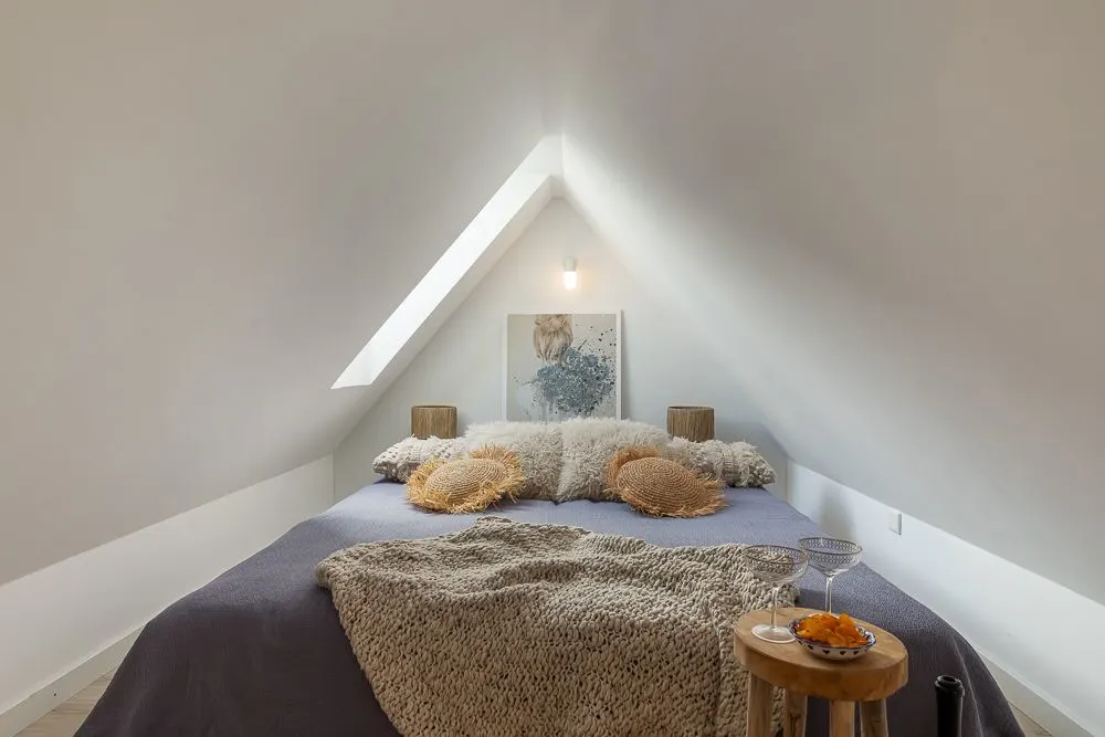 Gemütliches Schlafzimmer mit großem Bett unter einer schrägen Decke und Dachfenster.