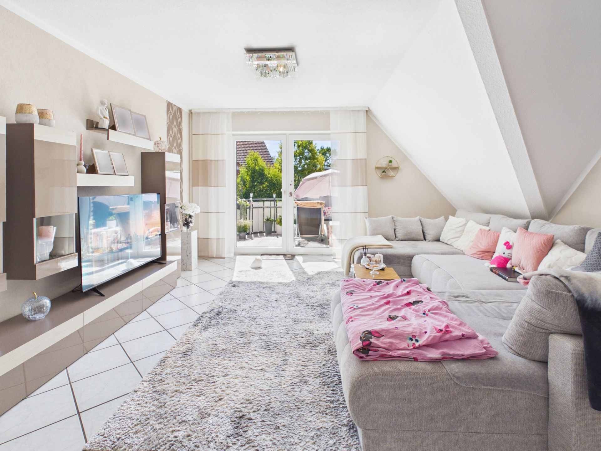 Helles Wohnzimmer mit Ecksofa, Teppich, TV-Wand und Zugang zu einem Balkon.