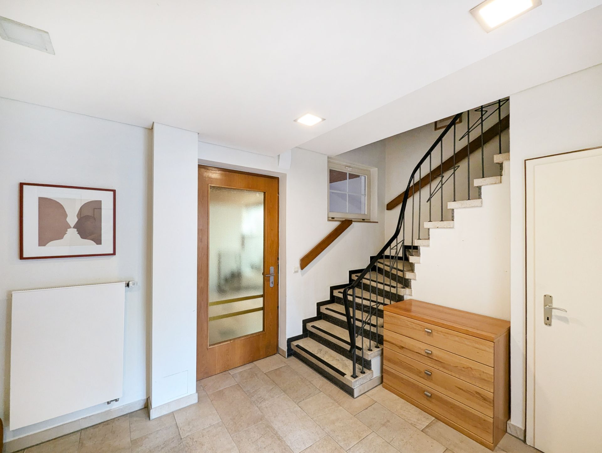 Heller Flur mit Treppe, Holztür, Kommode und Wandbild.