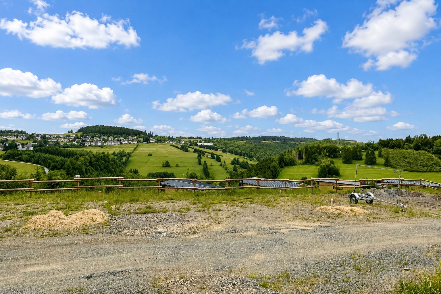 Blick auf eine grüne Hügellandschaft mit einzelnen Häusern und einem Holzzaun im Vordergrund.