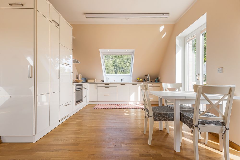 Helle Wohnküche mit Einbauküche, Esstisch und vier Stühlen, großes Fenster mit Blick ins Grüne.