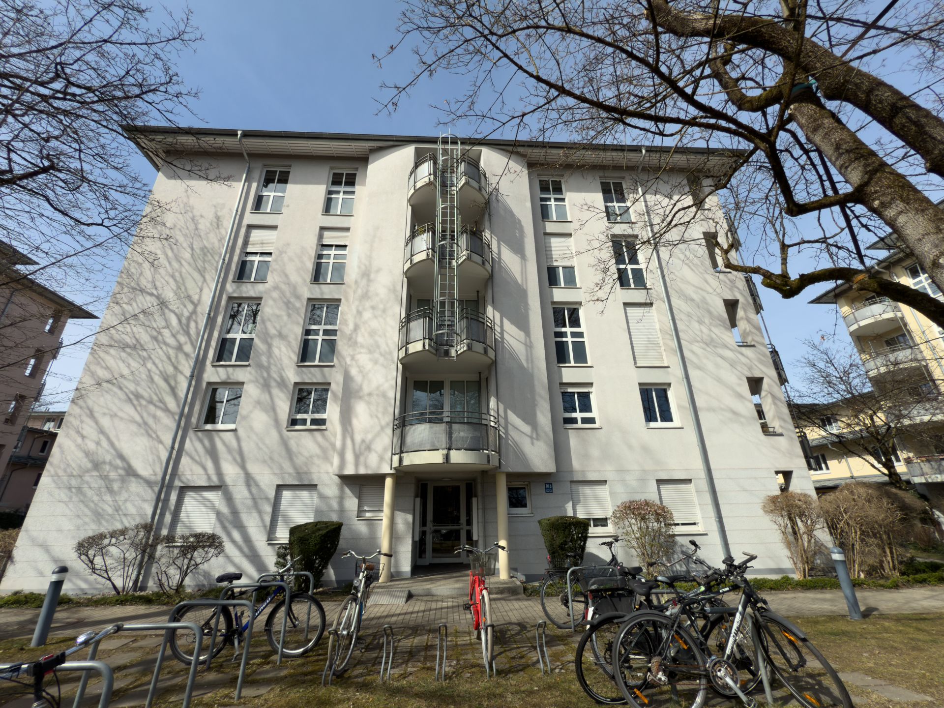 Mehrstöckiges Wohnhaus mit Balkonen, davor Fahrradständer und Fahrräder.