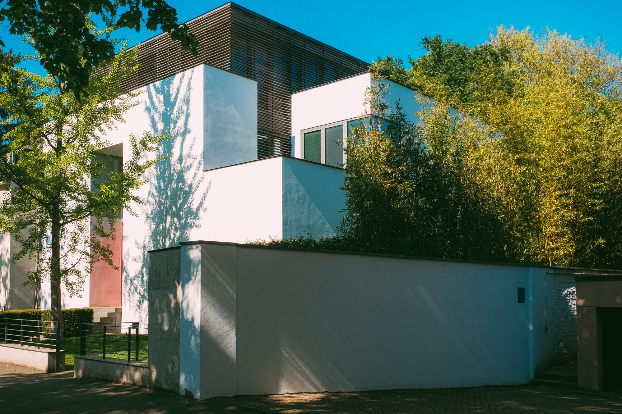 Modernes Wohnhaus mit weißen Fassaden, umgeben von Bäumen und einer weißen Gartenmauer.