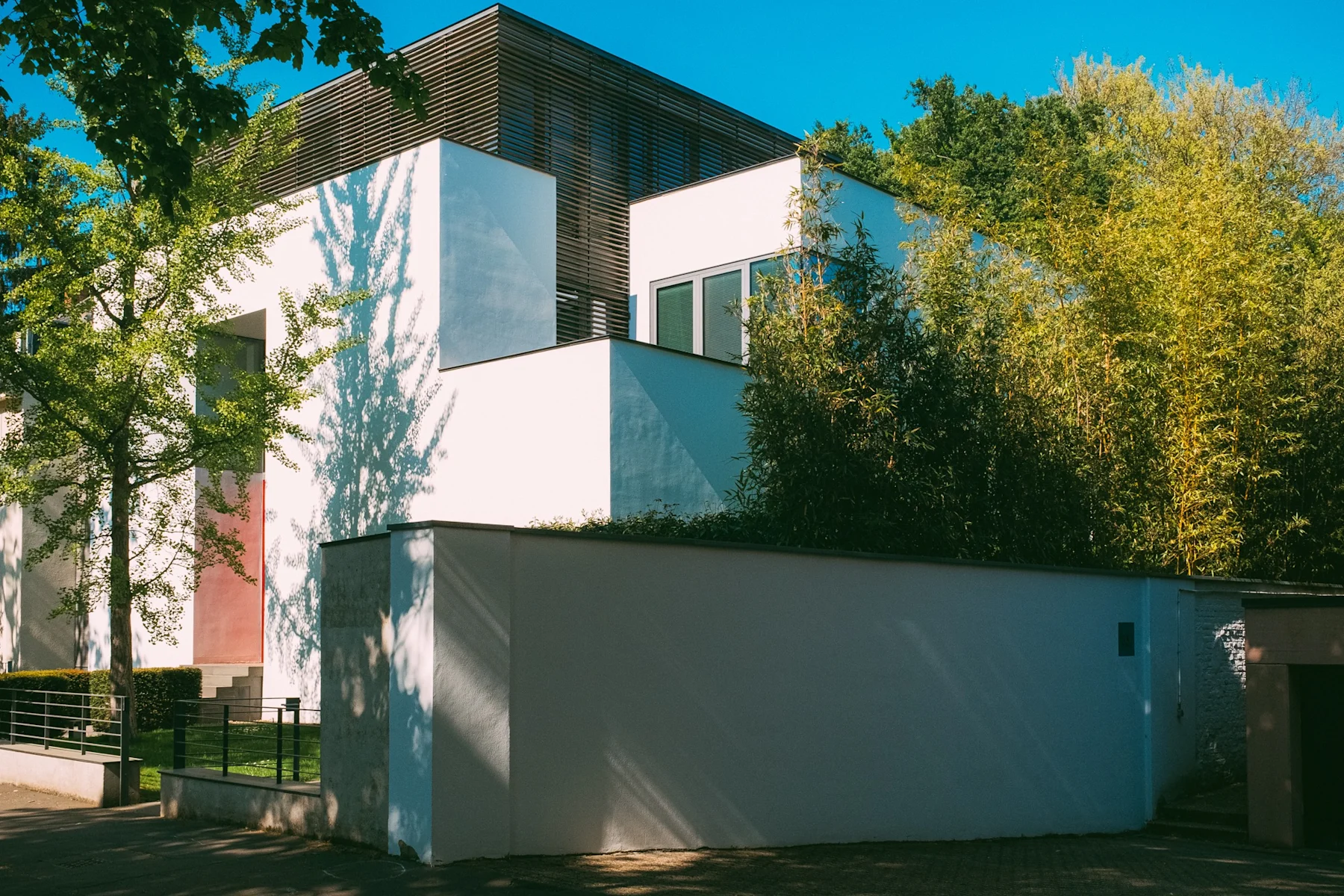 Modernes Wohnhaus mit weißen Fassaden, umgeben von Bäumen und einer weißen Gartenmauer.