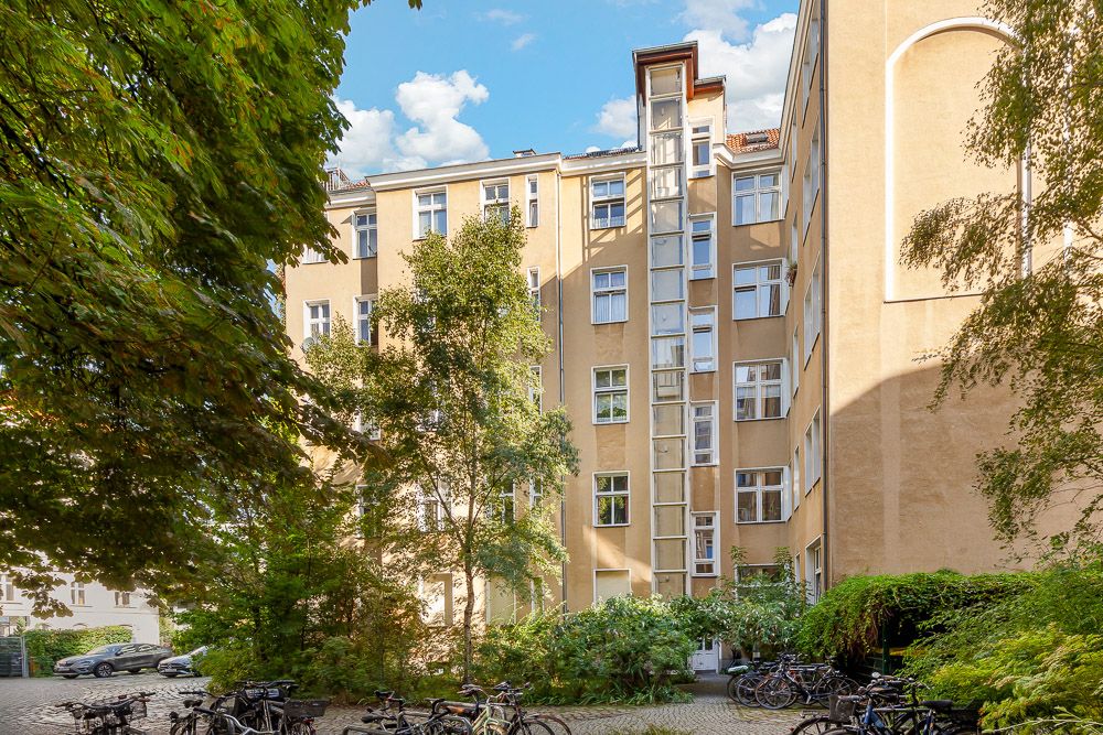 Mehrstöckiges Wohnhaus mit gelber Fassade, Bäumen und Fahrradständern im Innenhof.