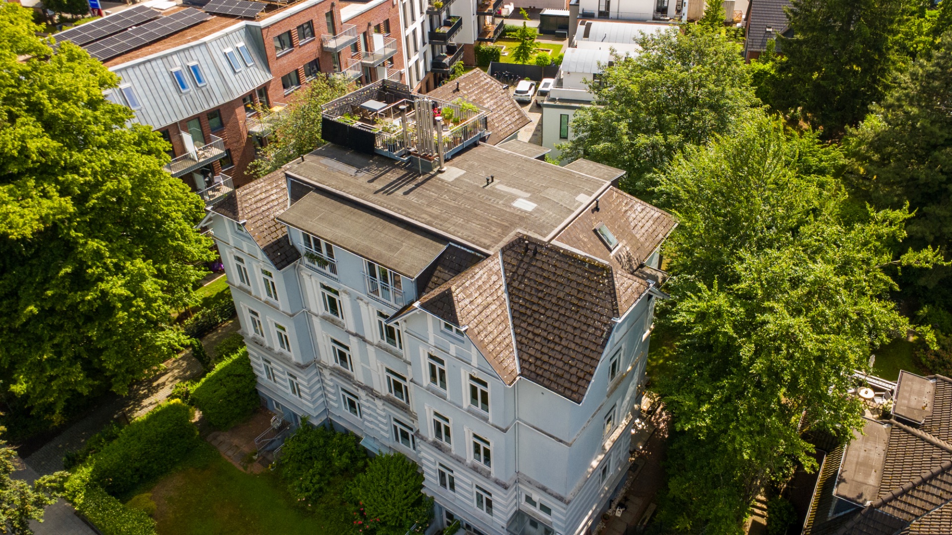 Mehrstöckiges Wohnhaus mit Flachdach und Dachterrasse, umgeben von Bäumen.