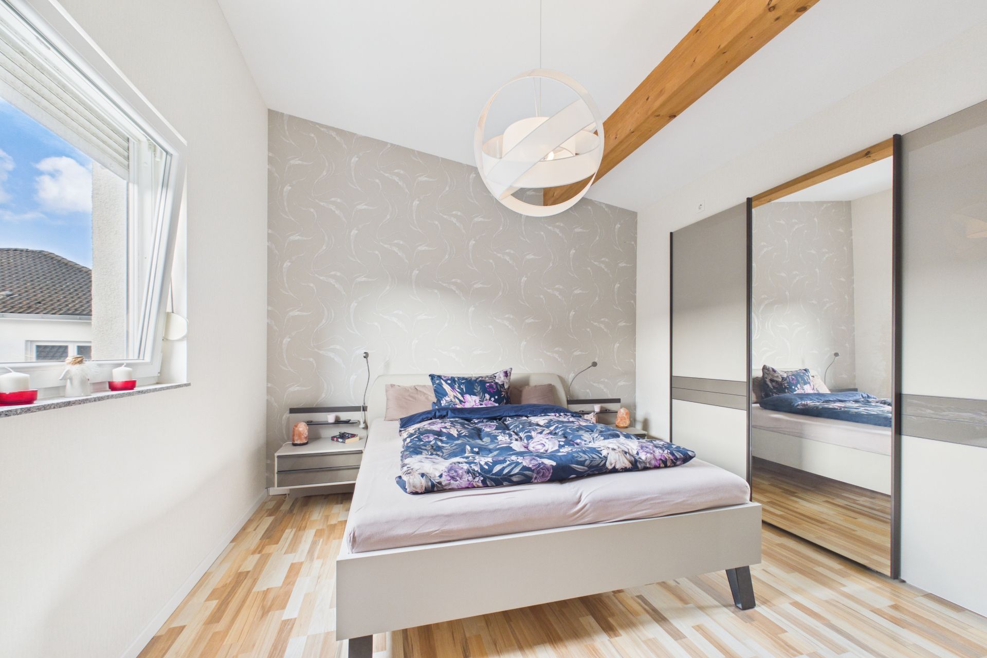 Helles Schlafzimmer mit Doppelbett, großem Spiegel-Kleiderschrank und Fenster.