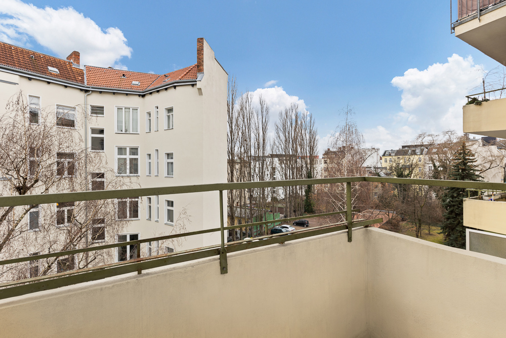 Blick von einem Balkon auf einen Innenhof mit Bäumen und Wohngebäuden.