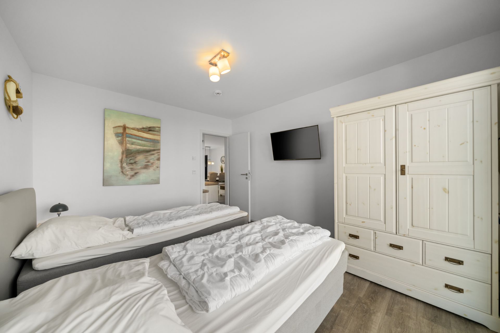 Schlafzimmer mit zwei Einzelbetten, weißem Kleiderschrank, Wandbild und Fernseher an der Wand.