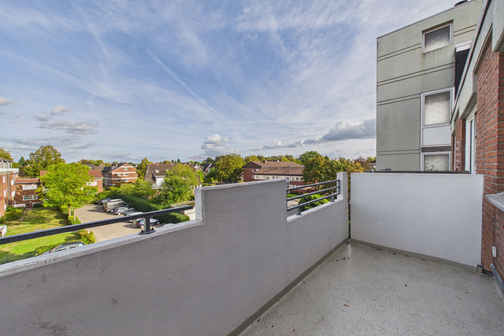 Balkon mit Blick auf Wohnhäuser, Bäume und blauen Himmel mit Wolken.
