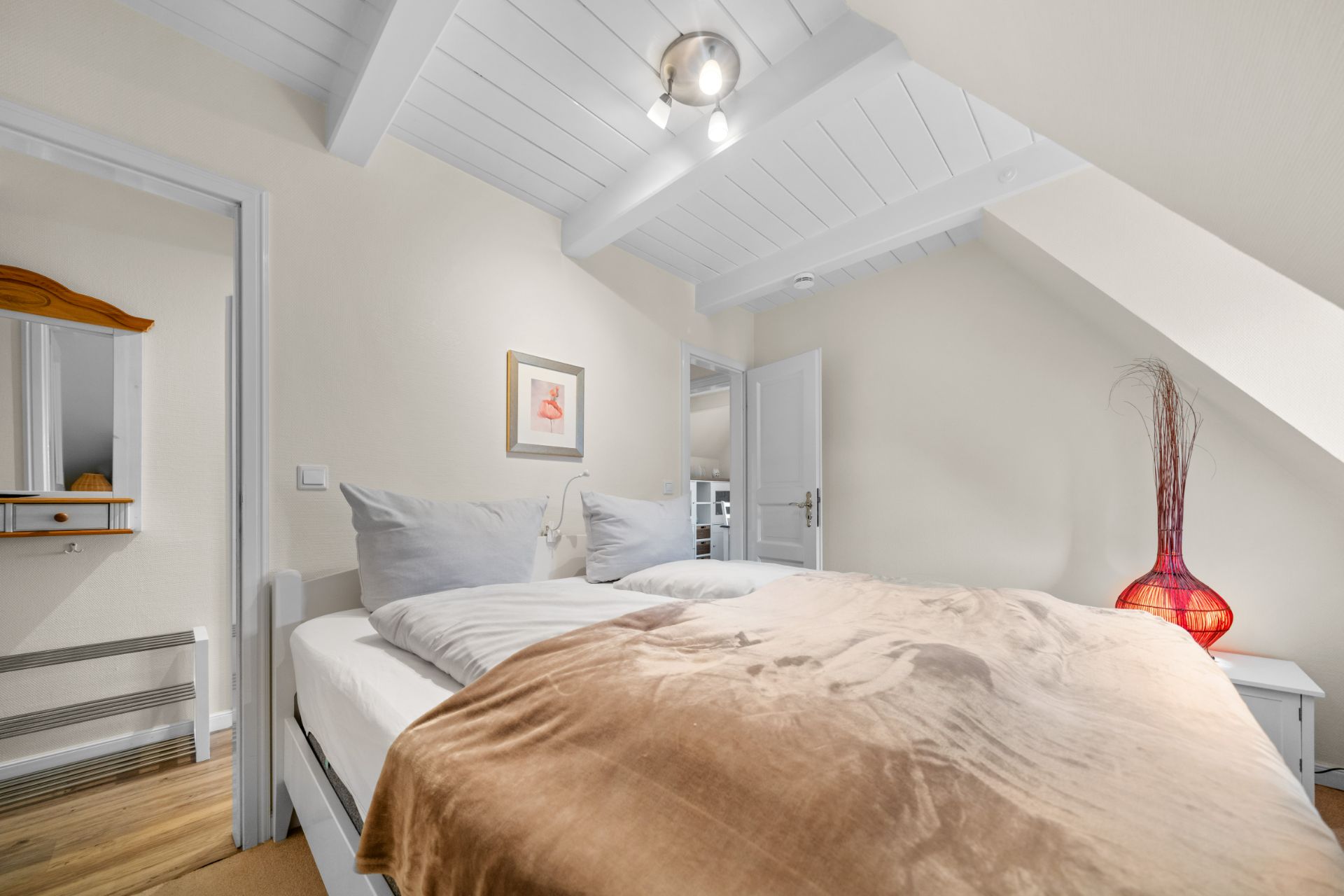 Schlafzimmer mit Doppelbett, weißer Decke, Holzboden und roter Dekovase in einer Wohnimmobilie.