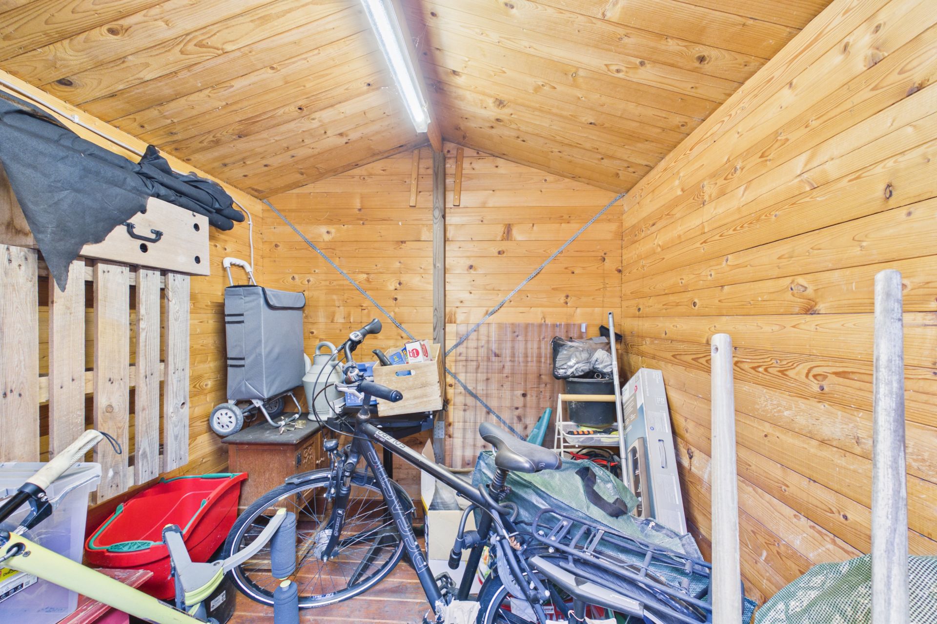Holzgartenhaus mit Fahrrädern, Werkzeug und verschiedenen Gegenständen, von innen fotografiert.