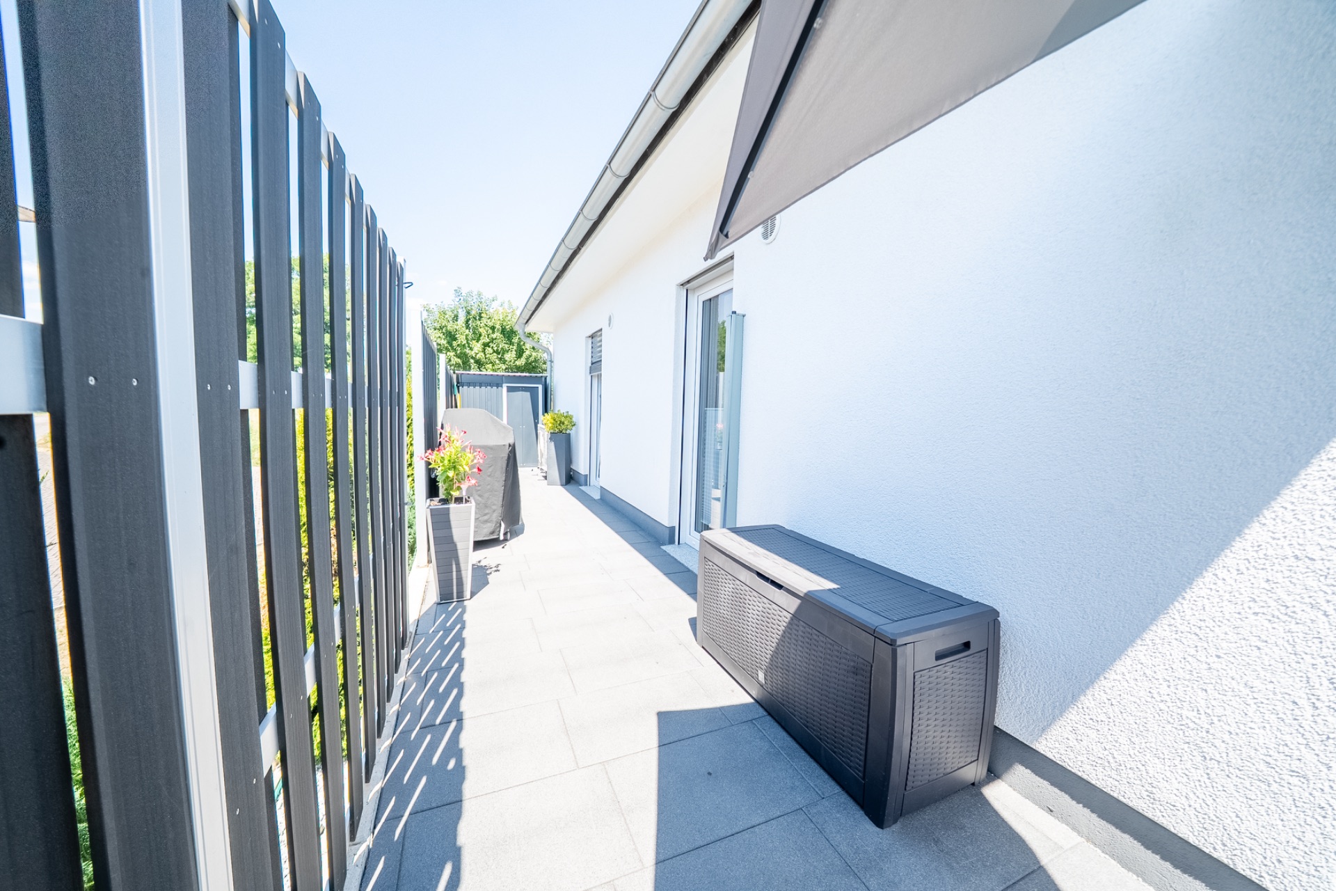 Helle Terrasse mit Pflanzkübeln, Bank und Sichtschutzzaun an einem Wohnhaus.