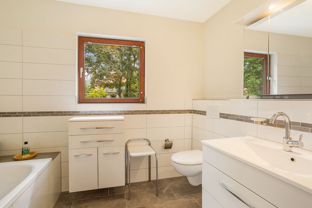 Modernes Badezimmer mit Fenster, Badewanne, Waschbecken, Toilette und weißen Möbeln.