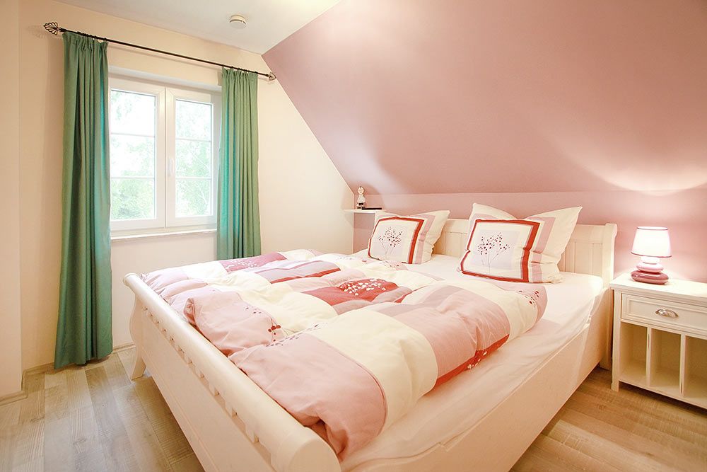 Helles Schlafzimmer mit Doppelbett, rosa Wänden, weißen Möbeln und grünem Vorhang am Fenster.