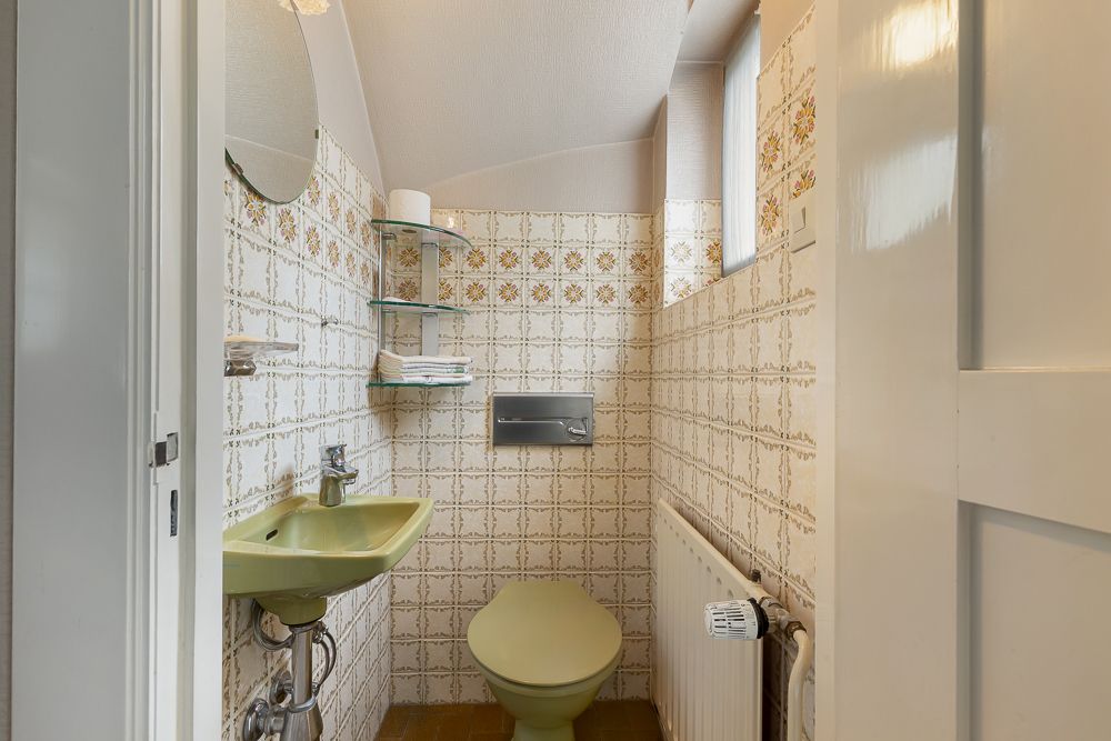 Kleines Badezimmer mit grünem Waschbecken, Toilette, Heizung und dekorativen Fliesen.