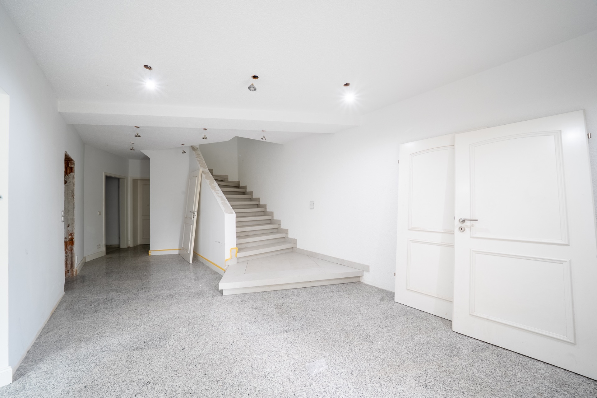 Heller Flur mit offenem Treppenaufgang und weißen Türen in einem Wohnhaus.