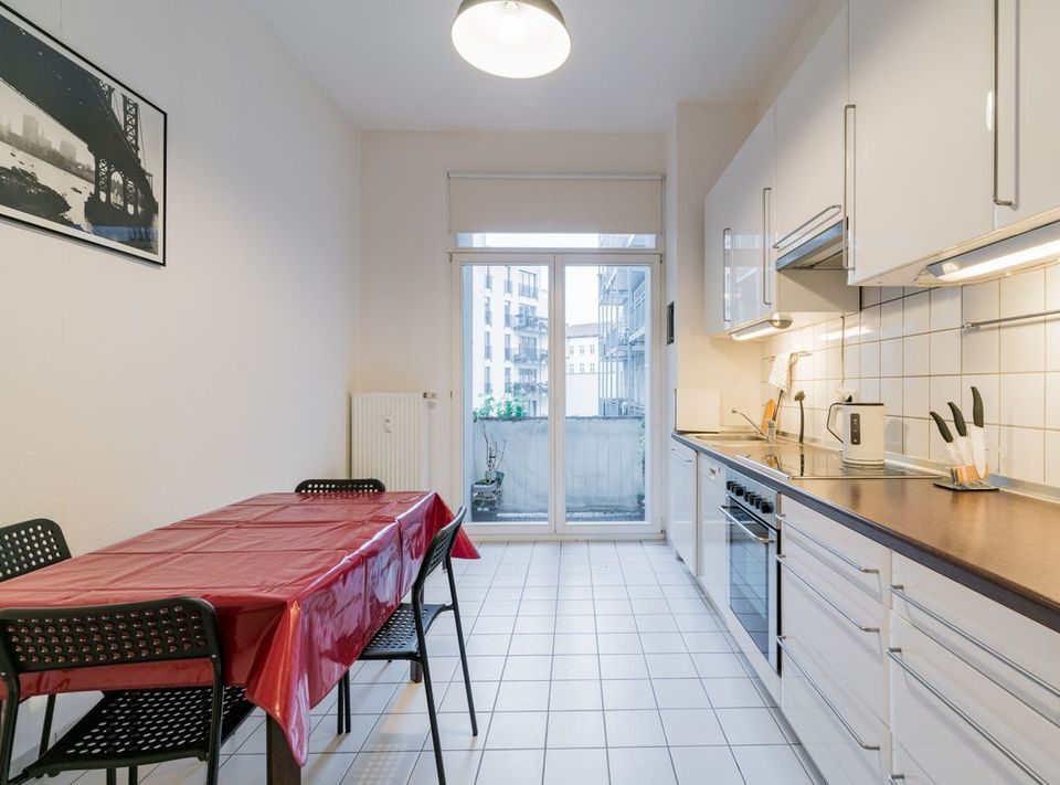 Helle Küche mit Esstisch, Stühlen, weißem Fliesenboden und Zugang zu einem Balkon.