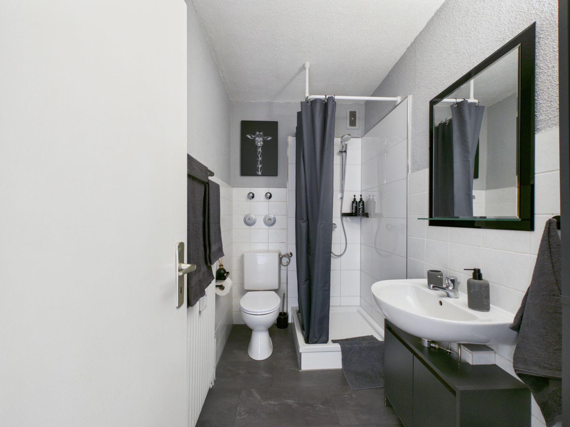 Modernes Badezimmer mit Dusche, WC, Waschbecken und Spiegel, Handtücher an der Wand.