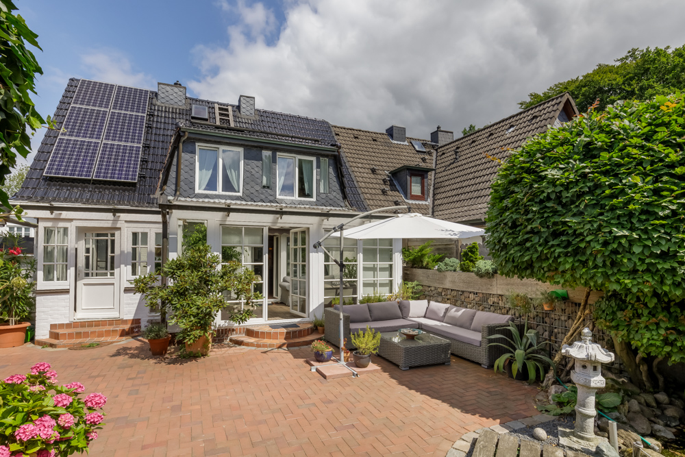 Hinterhof mit Terrasse, Sitzgruppe, Sonnenschirm, Pflanzen und Solarpanels auf dem Dach.