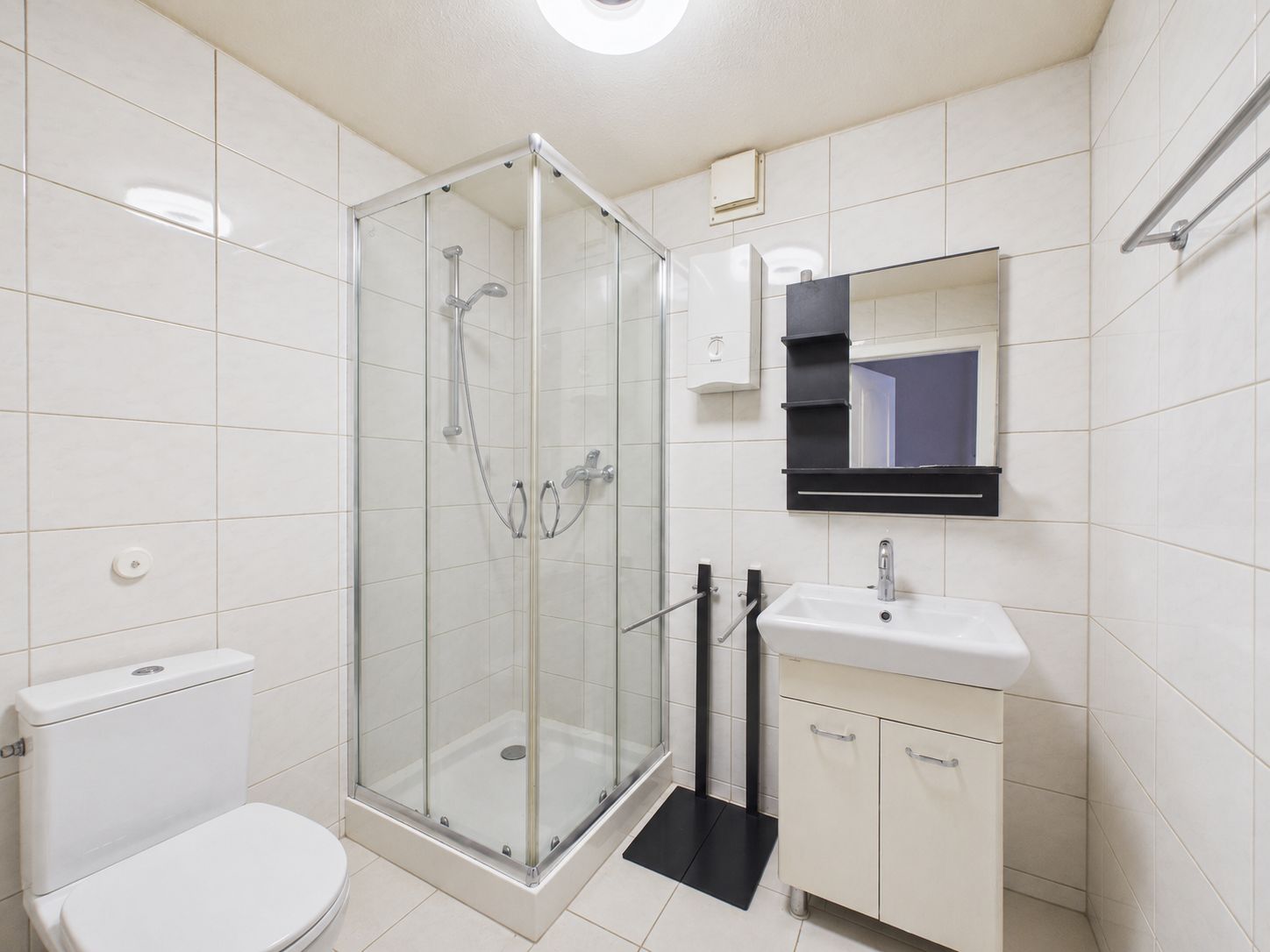 Modernes Badezimmer mit Dusche, Toilette, Waschbecken und Spiegel auf weißen Fliesen.