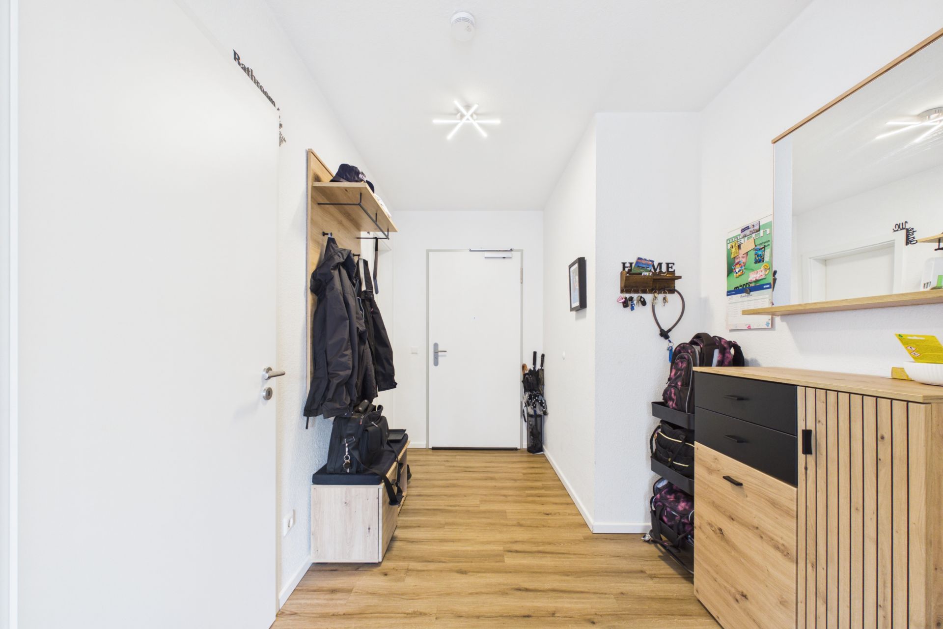 Heller Flur mit Garderobe, Holzboden, Kommode und Spiegel.