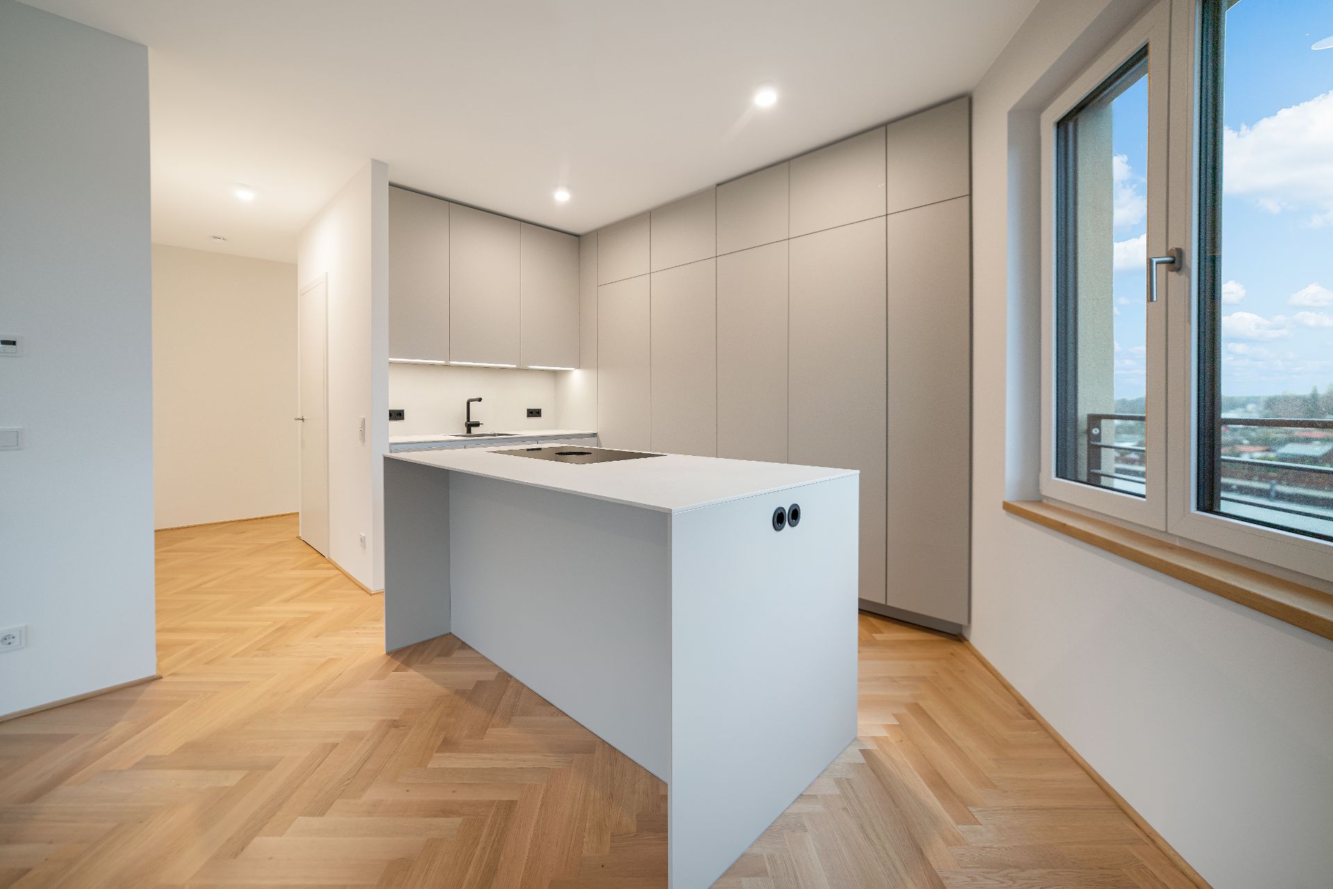 Moderne, helle Einbauküche mit Kücheninsel und großem Fenster, Parkettboden.