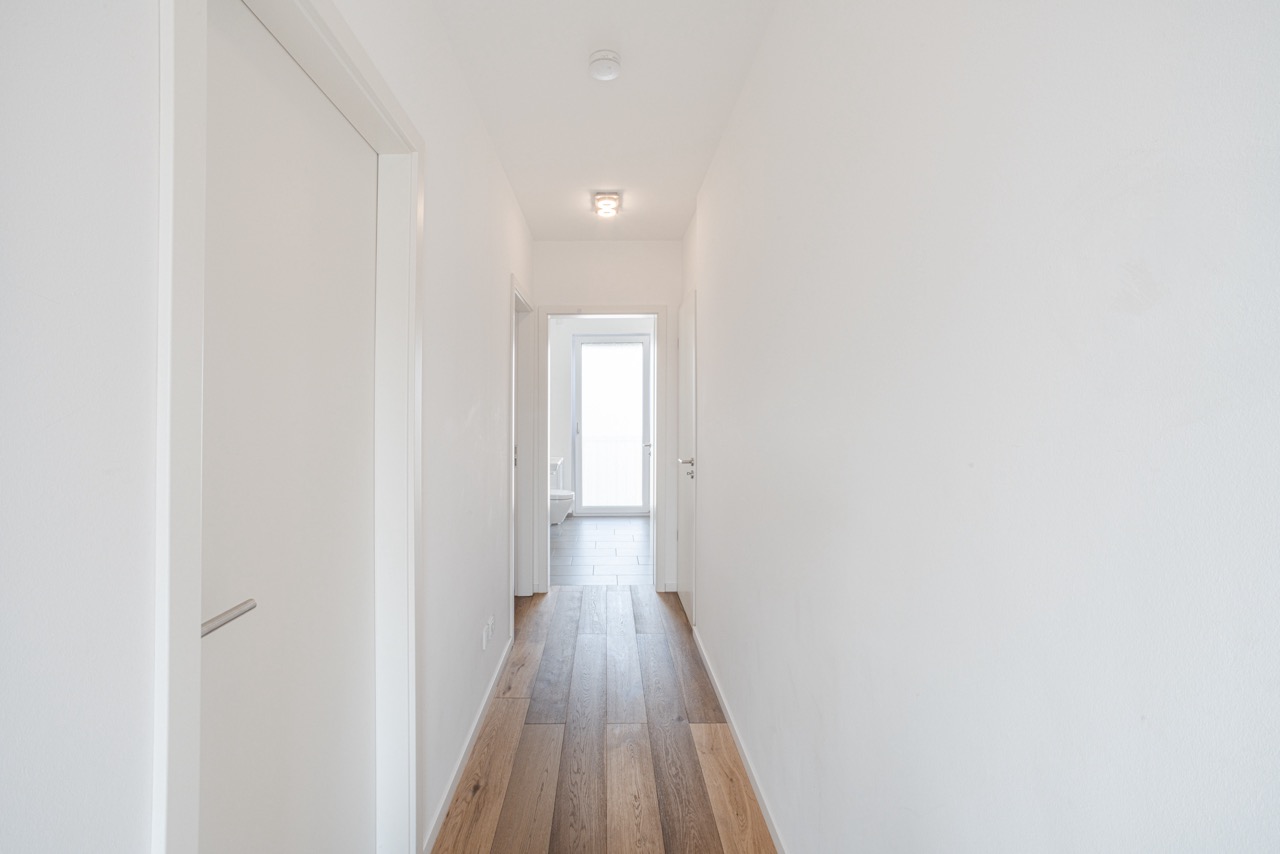 Heller Flur mit weiß gestrichenen Wänden und Holzfußboden, Türen zu beiden Seiten.