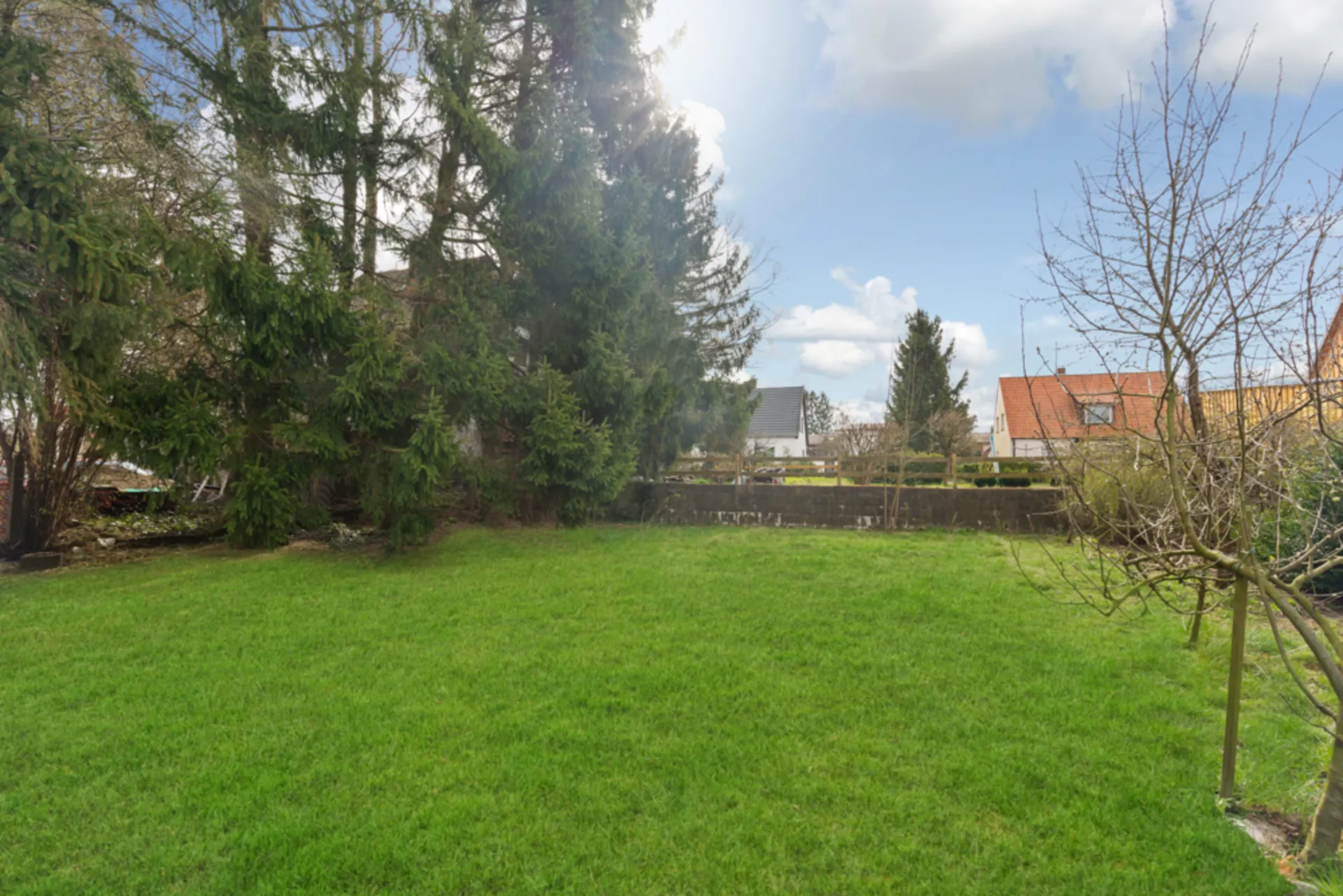 Grüner Garten mit Rasenfläche, Bäumen und Blick auf umliegende Häuser bei Tageslicht.