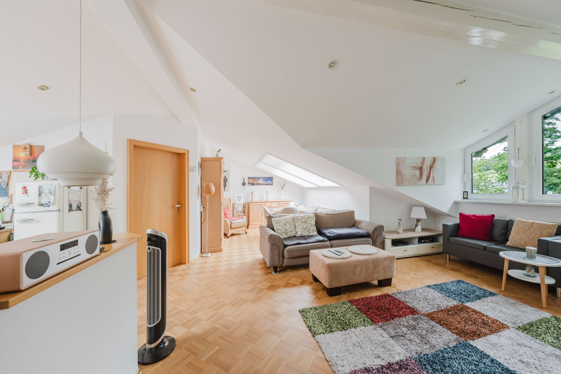 Wohnzimmer mit buntem Teppich, zwei Sofas, Tisch und großen Fenstern unter Dachschrägen.
