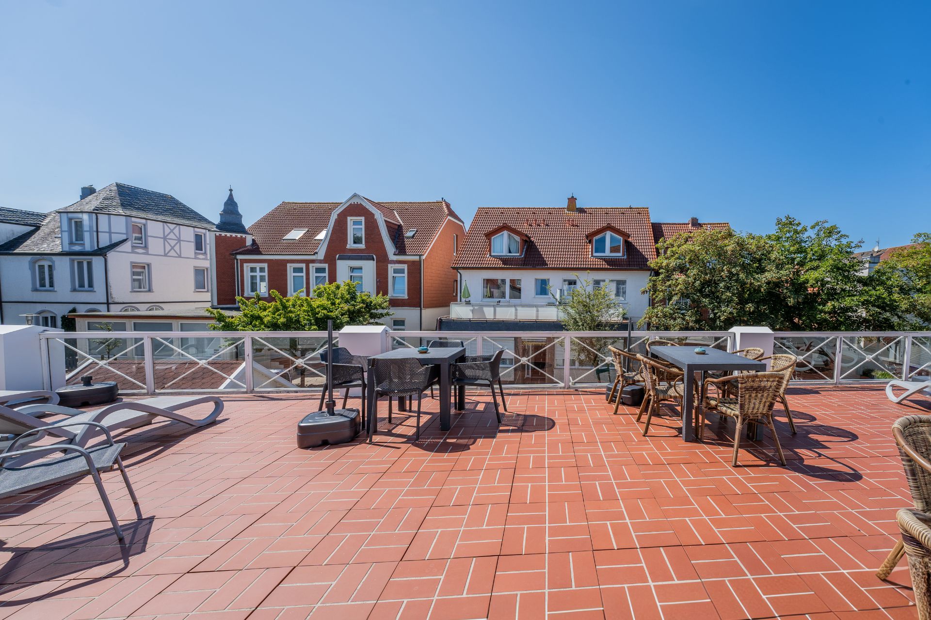 Große Terrasse mit roten Fliesen, Tischen, Stühlen und Blick auf Wohnhäuser.