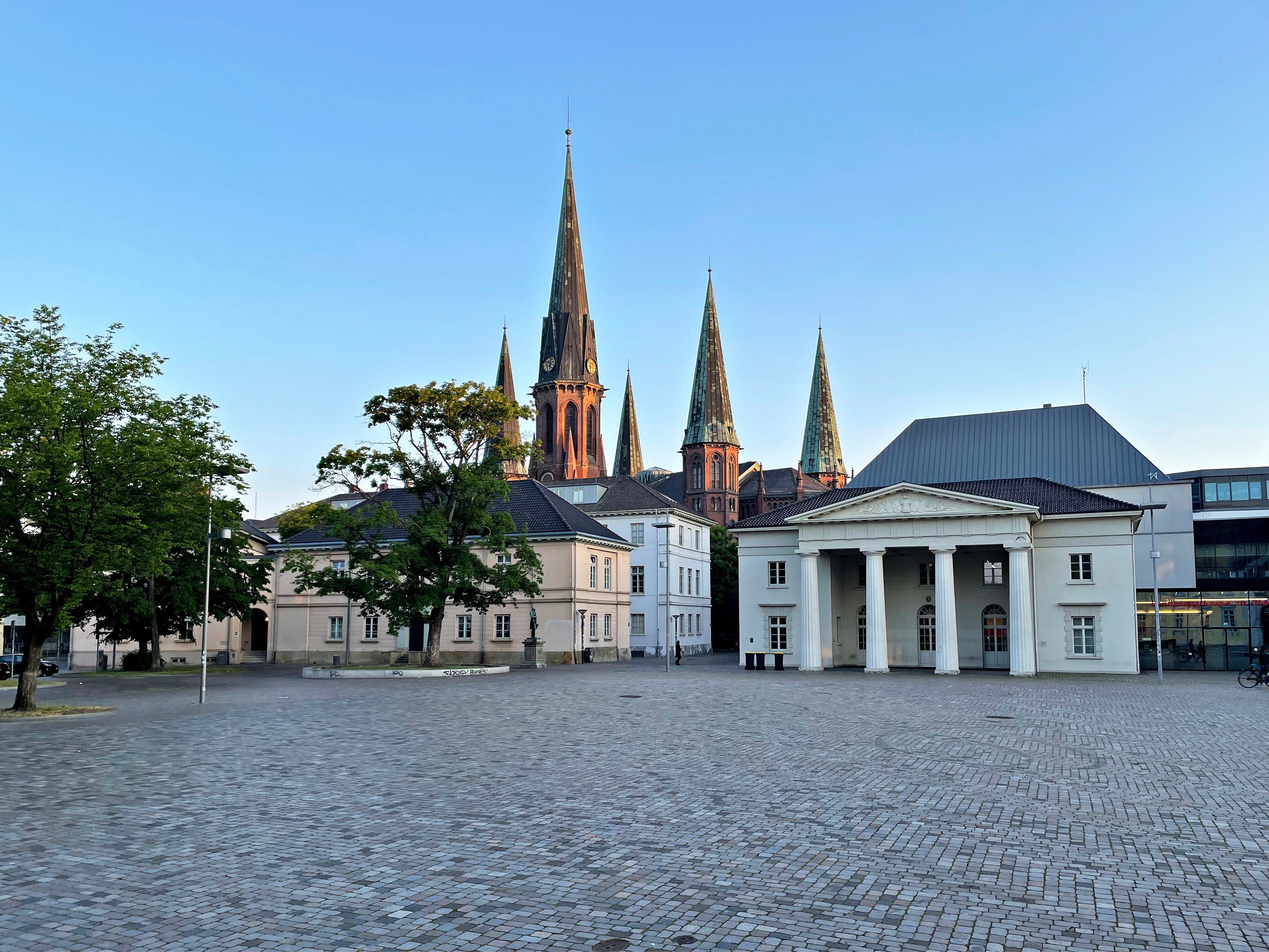 Teich mit Bäumen und einer Kirche im Hintergrund an einem sonnigen Tag.