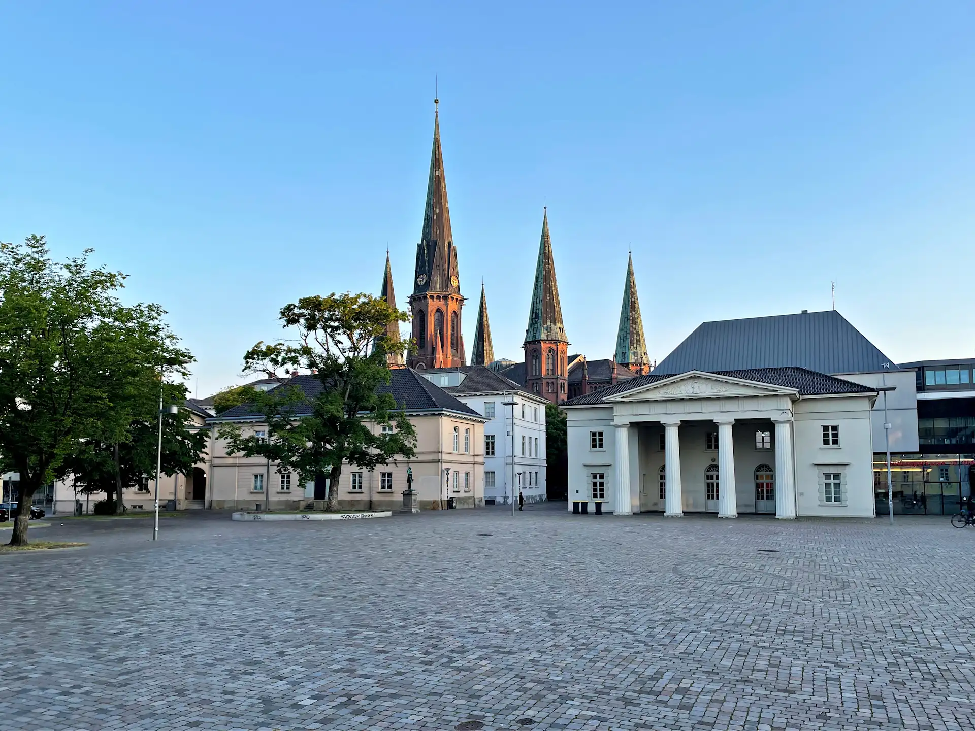 Teich mit Bäumen und einer Kirche im Hintergrund an einem sonnigen Tag.