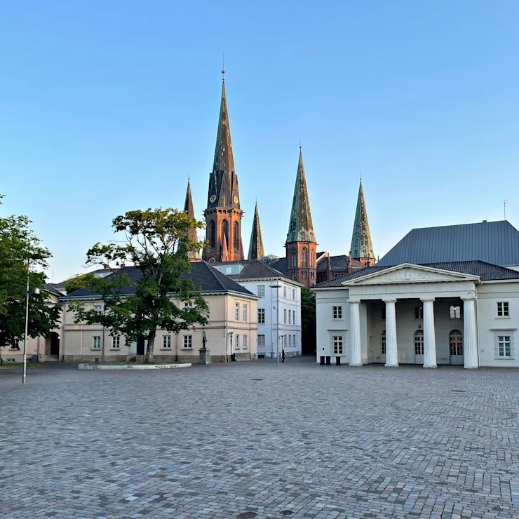 Teich mit Bäumen und einer Kirche im Hintergrund an einem sonnigen Tag.