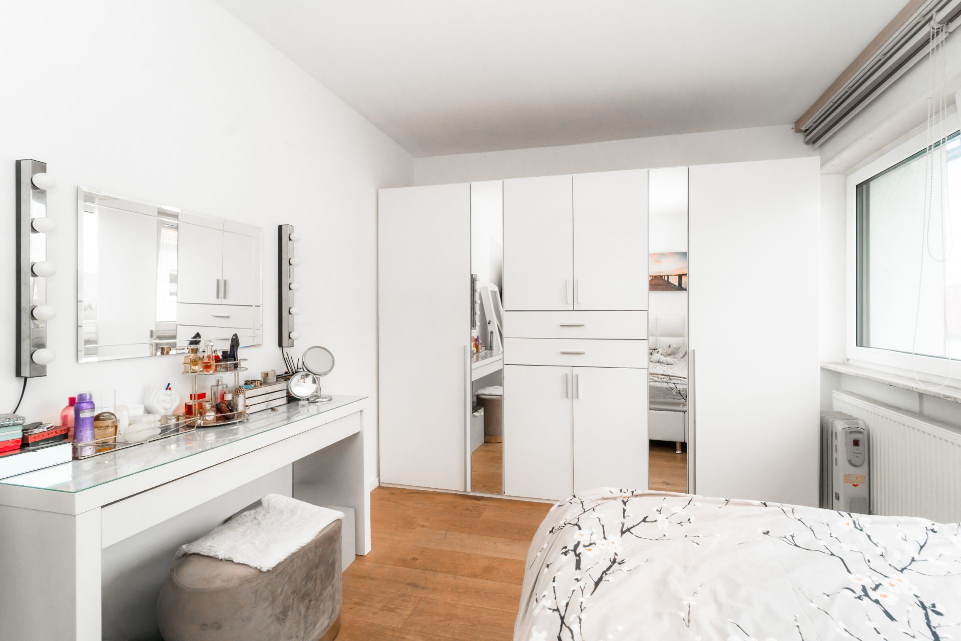 Helles Schlafzimmer mit weißem Kleiderschrank, Schminktisch und großem Fenster.