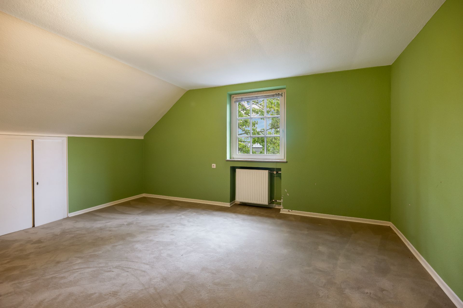 Leeres Zimmer mit grünen Wänden, Fenster und Teppichboden.
