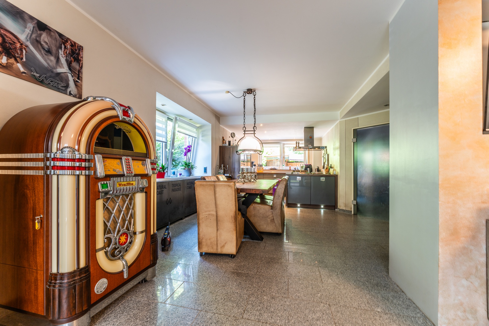 Wohnküche mit Esstisch, Stühlen, Jukebox und großen Fenstern, modernes Design.
