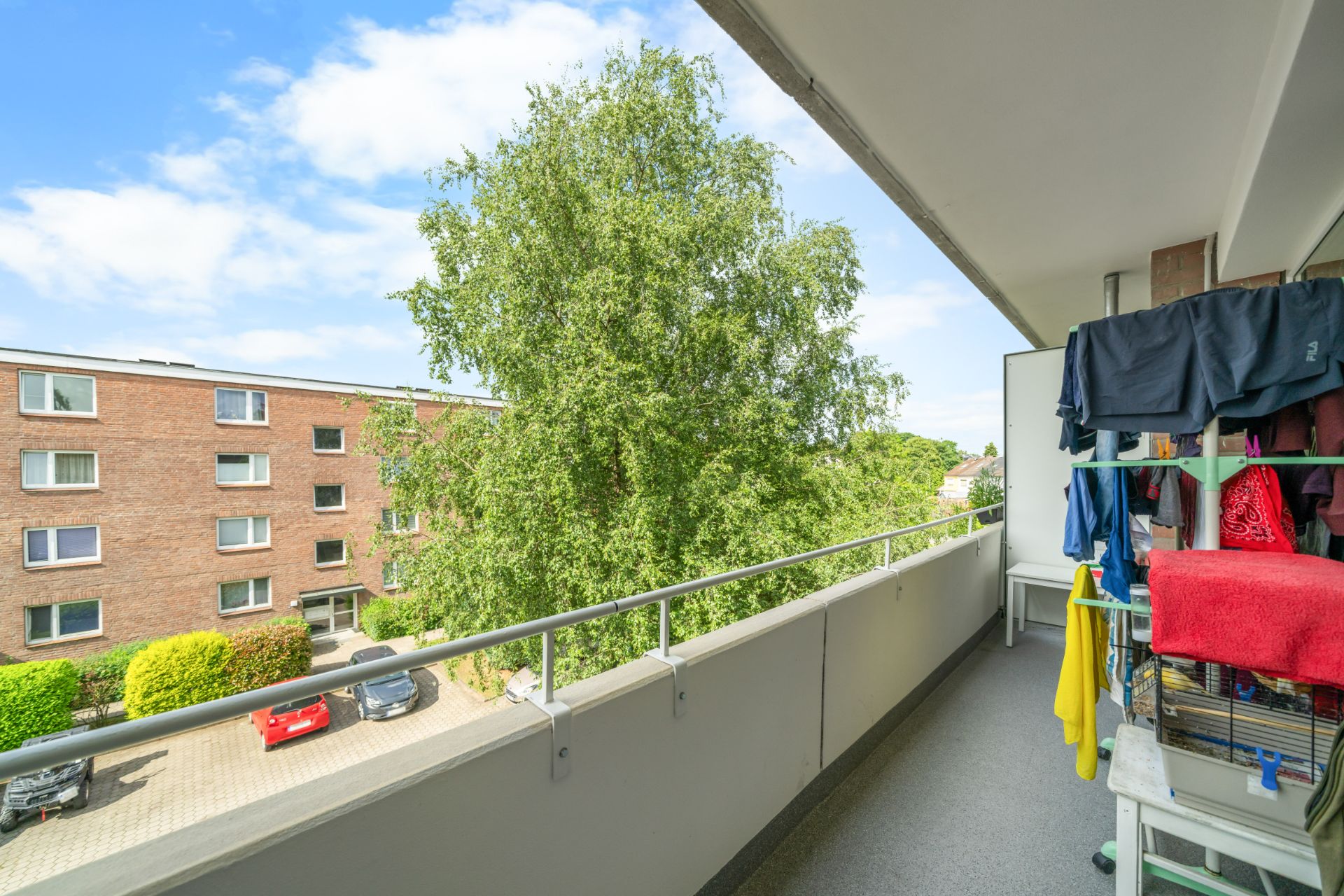Balkon mit Wäscheständer, Blick auf einen Baum und ein Mehrfamilienhaus.