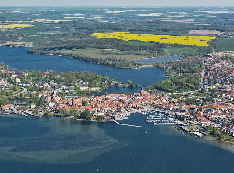 Luftaufnahme einer Stadt mit Häusern, Wasserflächen und umliegenden Feldern.