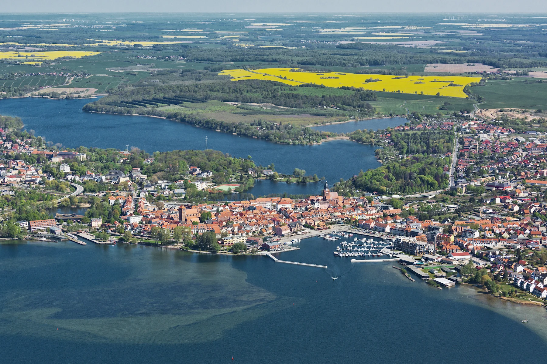Luftaufnahme einer Stadt mit Häusern, Wasserflächen und umliegenden Feldern.