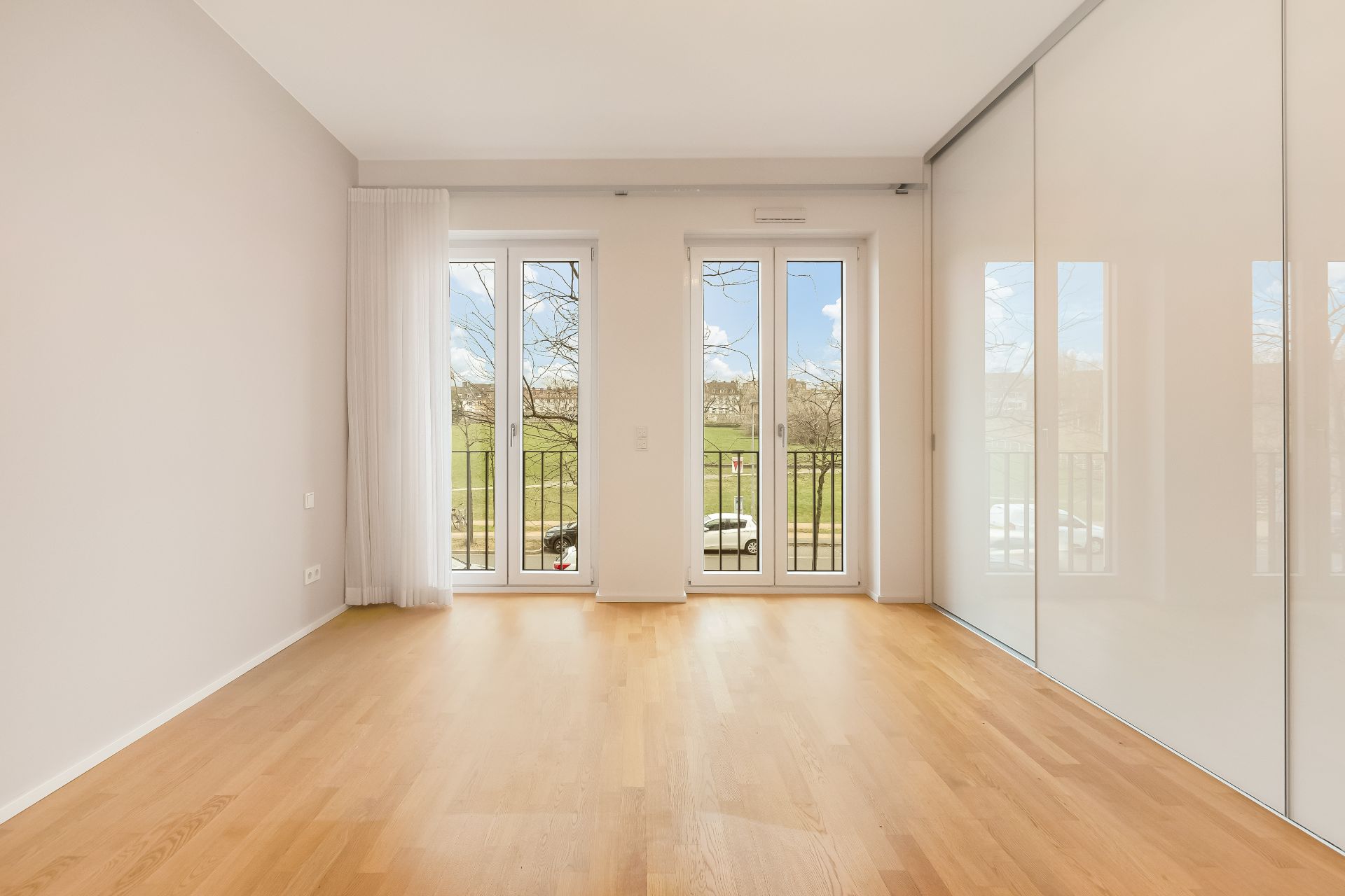 Heller Raum mit Holzboden, großen Fenstern und Blick nach draußen.
