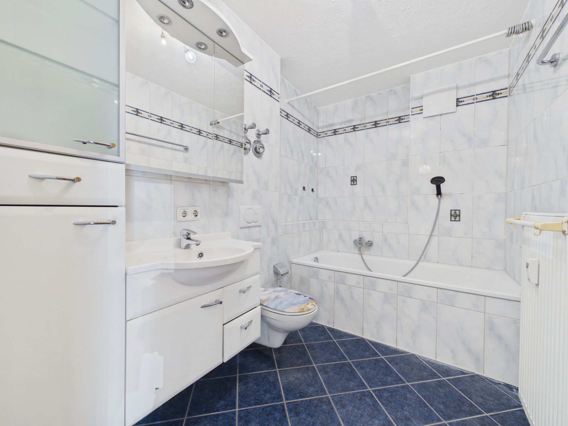 Helles Badezimmer mit Badewanne, Waschbecken, Toilette und weißen Fliesen.
